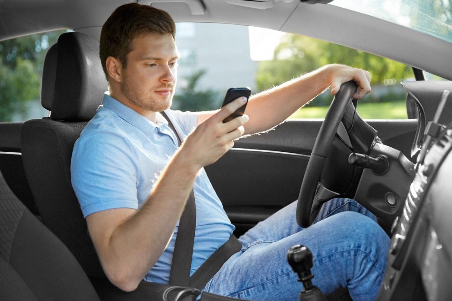 Young driver checking a rental car booking on his phone from behind the wheel